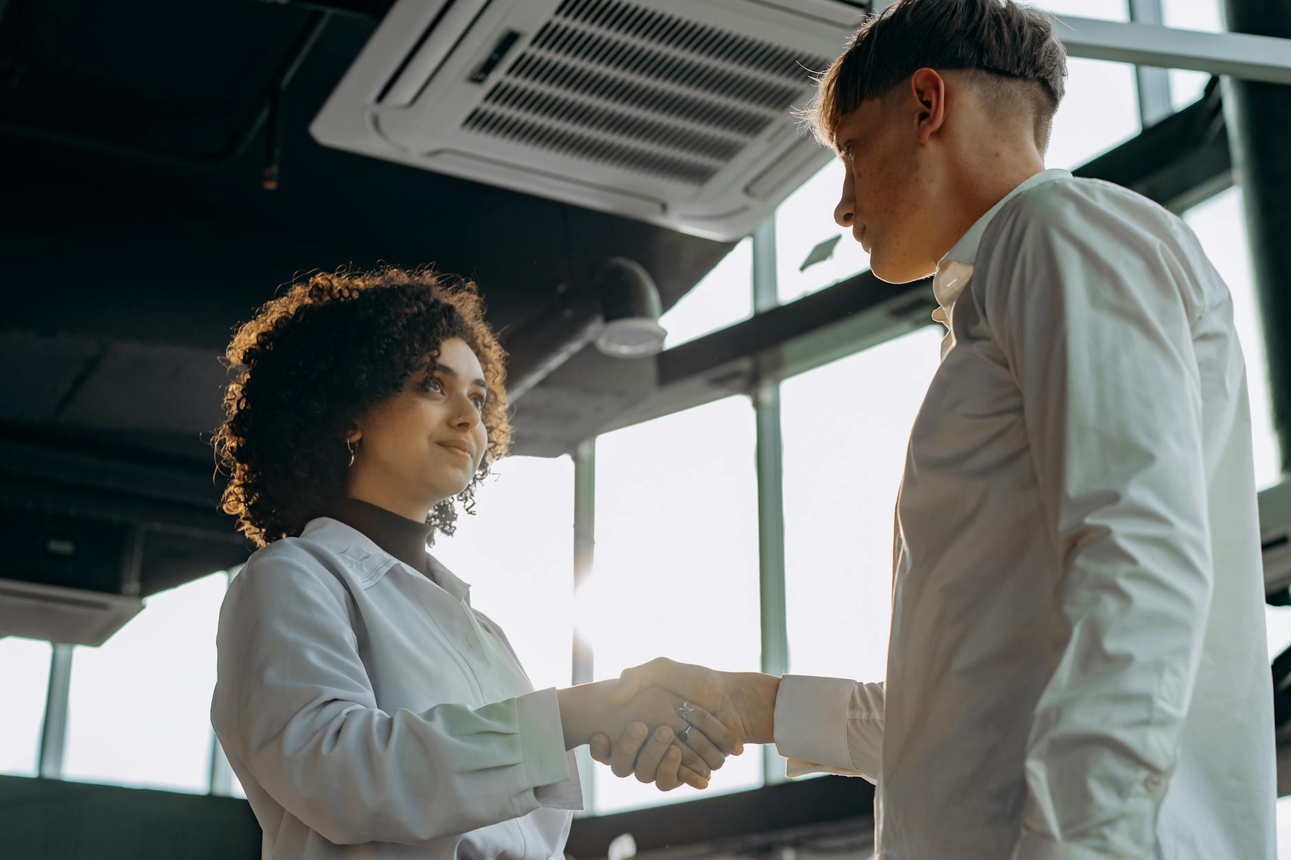 Two professionals shaking hands in a modern office setting.
